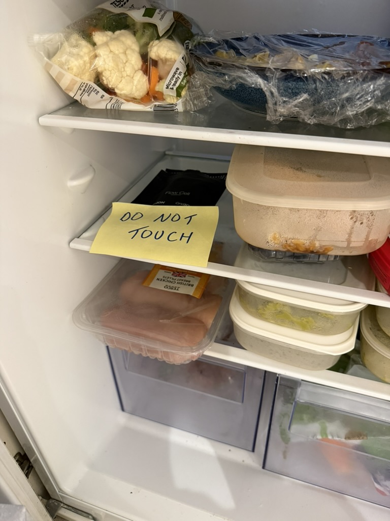 Inside a domestic fridge, a box of flow cells on the middle shelf behind a yellow sticky note reading 'DO NOT TOUCH'.