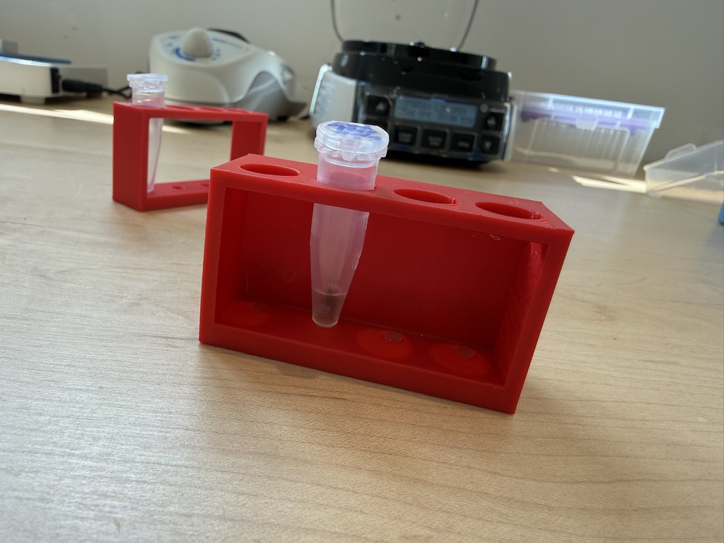 Two red 3D-printed magnetic racks for 1.5 mL tubes on the kitchen bench, one holding a tube mid-bead-wash.