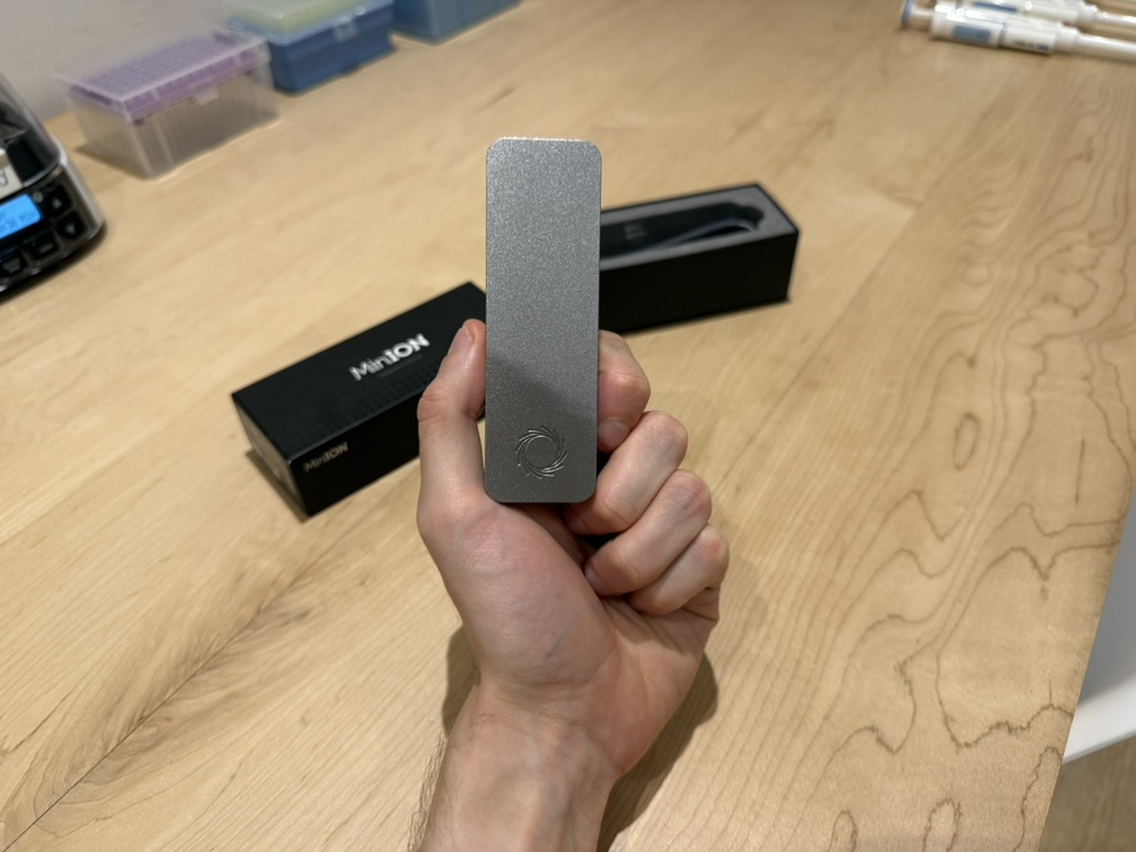 A MinION Mk1B held in the author's hand next to its black packaging box.